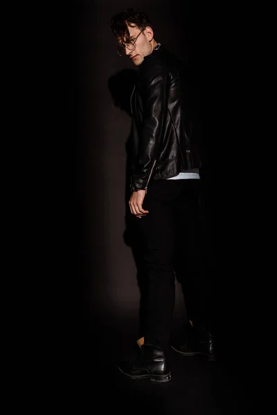 Hombre con estilo en gafas y chaqueta de cuero de pie en negro - foto de stock