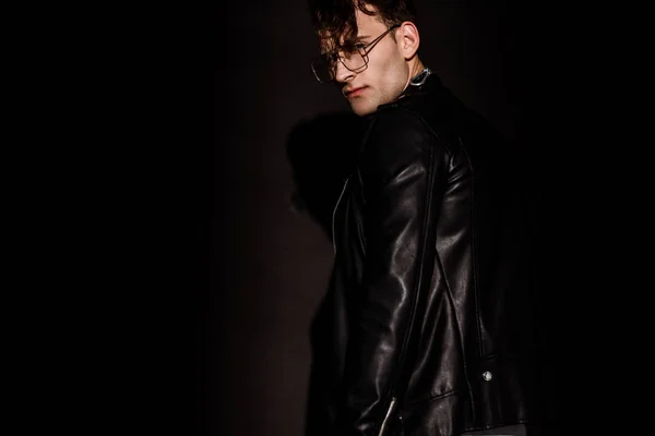 Trendy man in glasses and leather jacket standing on black — Stock Photo