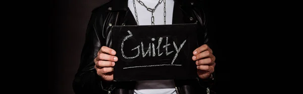 Panoramic shot of man holding chalk board with guilty lettering on black — Stock Photo