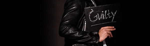 Panoramic shot of man holding chalk board with guilty letters on black — Stock Photo