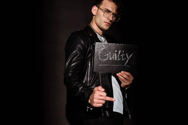 Handsome man in glasses holding chalk board with guilty lettering on black — Stock Photo