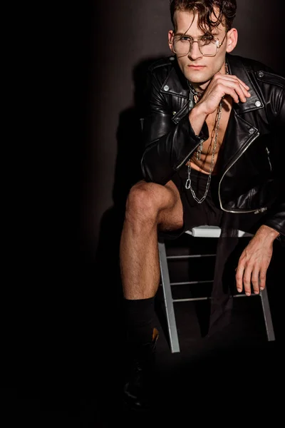 Brutal e sexy homem no couro jaqueta sentado no preto — Fotografia de Stock