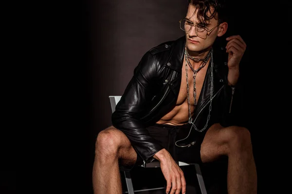 Nachdenklicher junger Mann in Lederjacke sitzt auf schwarz — Stockfoto