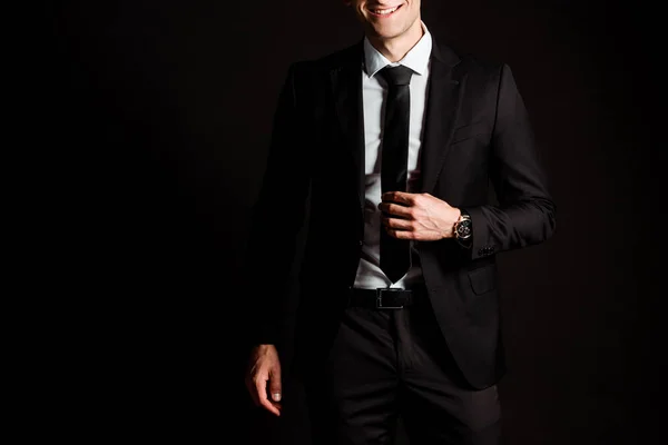 Cropped view of happy businessman touching tie isolated on black — Stock Photo