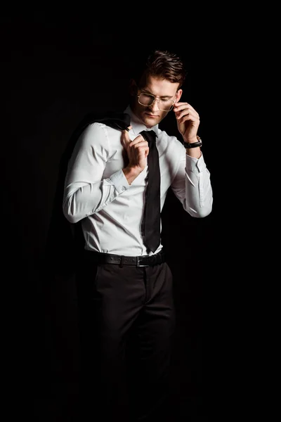 Handsome man touching glasses isolated on black — Stock Photo