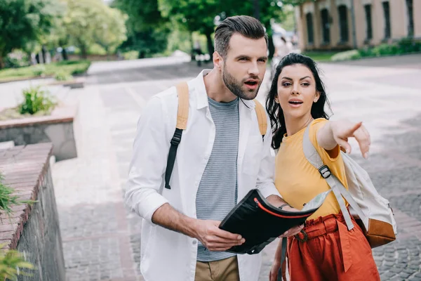 Attractive woman pointing with finger while standing near bearded man with map — Stock Photo