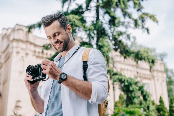 Vista de ángulo bajo del hombre barbudo alegre que sostiene la cámara digital - foto de stock