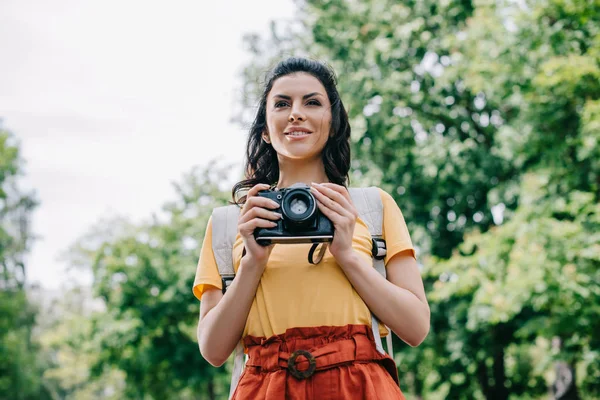 Joyeuse jeune femme tenant appareil photo numérique à l'extérieur — Photo de stock