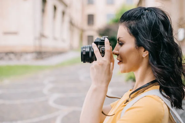 Side view of attractive girl holding digital camera while taking photo — Stock Photo