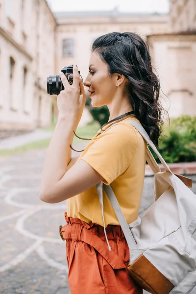 Vista lateral de la hermosa chica sosteniendo la cámara digital mientras toma la foto - foto de stock