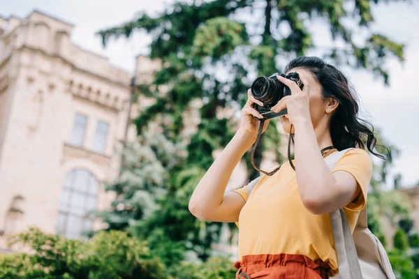 Низький кут зору дівчини, що тримає цифрову камеру під час фотографування — стокове фото