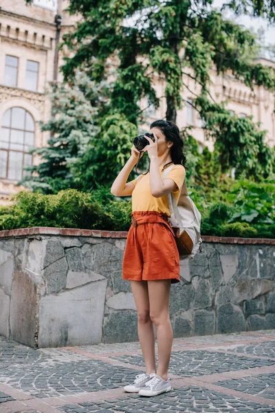 Дівчина тримає цифрову камеру під час фотографії біля будівлі та дерев — стокове фото