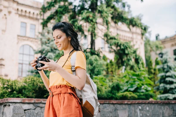 Menina segurando câmera digital perto de construção e árvores — Fotografia de Stock