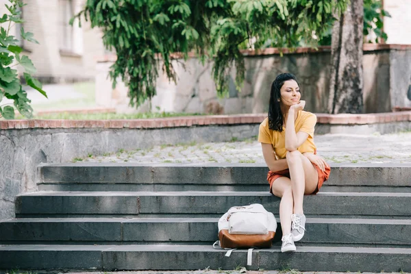 Attractive woman sitting near backpack on stairs — Stock Photo