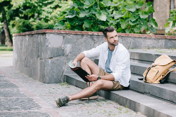 Handsome bearded traveler sitting on stairs and looking at map — Stock Photo