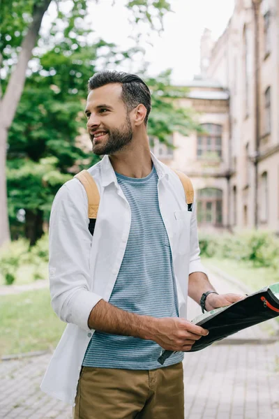 Schöner bärtiger Tourist lächelt, während er eine Karte in der Nähe des Gebäudes hält — Stockfoto