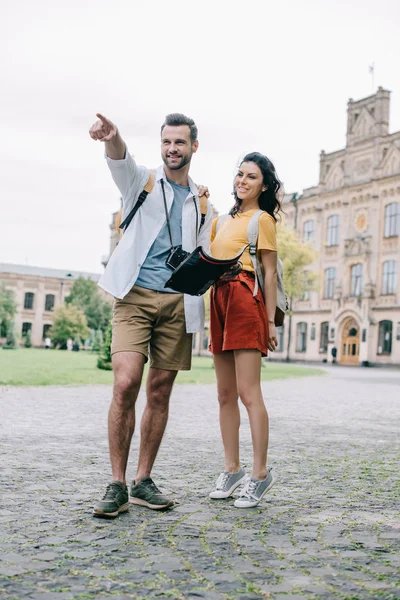 Schöner Mann, der mit dem Finger zeigt, während er Karte in der Nähe von Mädchen hält — Stockfoto