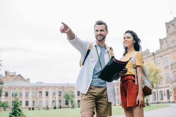 Hombre feliz señalando con el dedo mientras sostiene el mapa cerca de la mujer - foto de stock