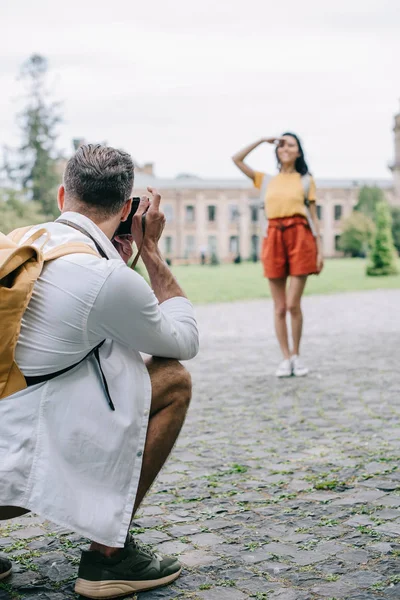 Selective focus of man taking photo of young woman standing near building — Stock Photo