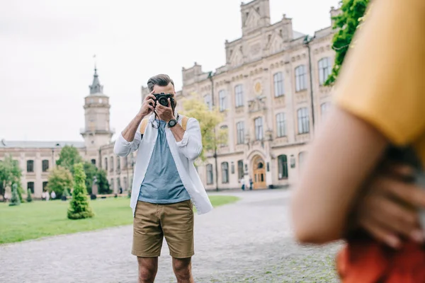 Selective focus of man covering face while taking photo of woman near university — Stock Photo