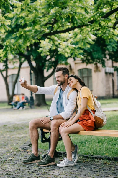 Счастливый мужчина делает селфи с веселой молодой женщиной на смартфоне — стоковое фото