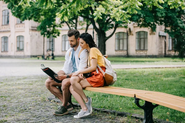 Handsome man and attractive woman sitting on bench with map — Stock Photo