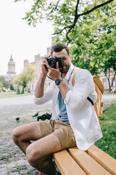 Бородатий чоловік сидить на дерев'яній лавці і фотографує — стокове фото