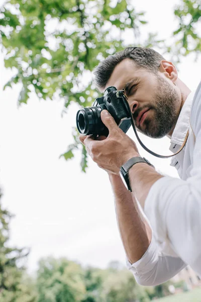 Low angle view of man covering face with digital camera and taking photo — Stock Photo