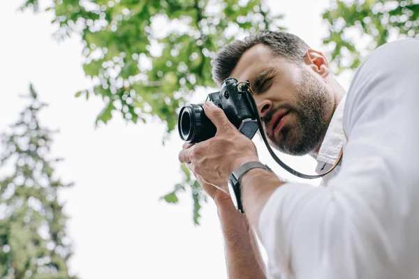 Низький кут зору людини, що покриває обличчя цифровою камерою і фотографується проти неба — стокове фото