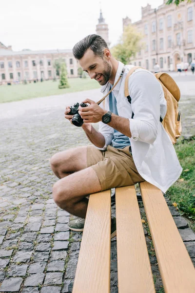 Foco seletivo do homem feliz olhando para a câmera digital enquanto sentado no banco — Fotografia de Stock