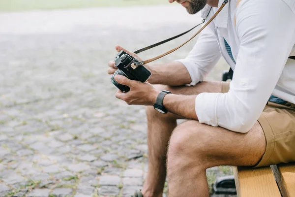 Cropped view of bearded man sitting on bench with digital camera — Stock Photo