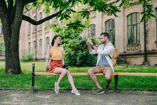 Hombre barbudo tomando fotos en el teléfono inteligente cerca de la mujer feliz - foto de stock