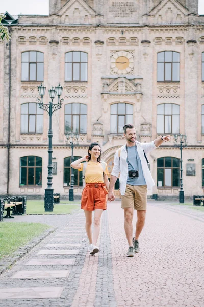 Guapo hombre apuntando con el dedo mientras toma de la mano con chica - foto de stock