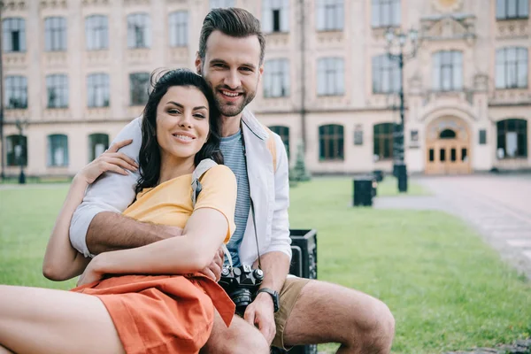 Glückliches Paar blickt in die Kamera, während es in der Nähe der Universität sitzt — Stockfoto