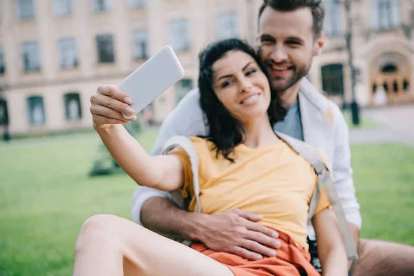 Selective focus of happy couple taking selfie near building — Stock Photo