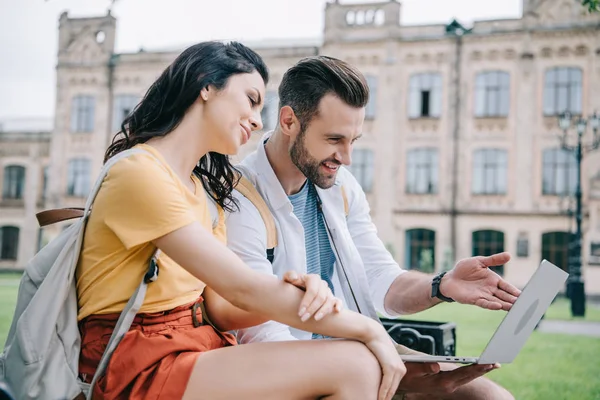 Attraente giovane donna seduta vicino barbuto uomo utilizzando il computer portatile — Foto stock