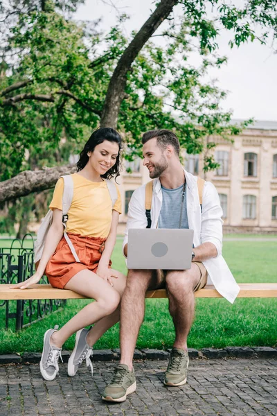 Jeune femme assise sur le banc près de l'homme en utilisant un ordinateur portable — Photo de stock