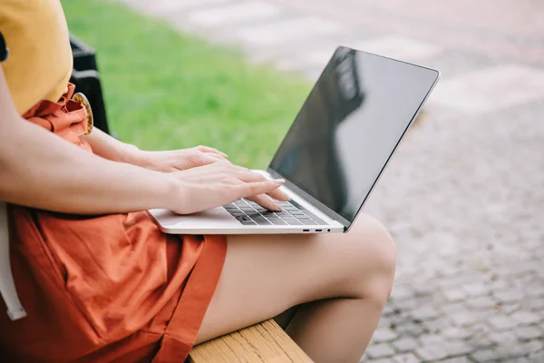 Vista ritagliata di ragazza seduta su panchina e utilizzando il computer portatile con schermo bianco — Foto stock