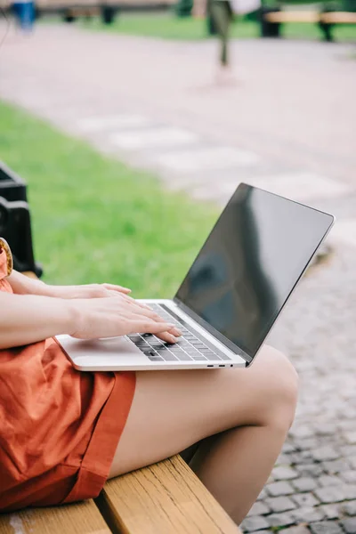 Vista cortada da mulher sentada no banco e usando laptop com tela em branco — Fotografia de Stock