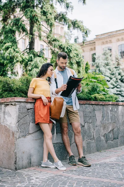 Bearded man and woman standing near building with atlas — Stock Photo