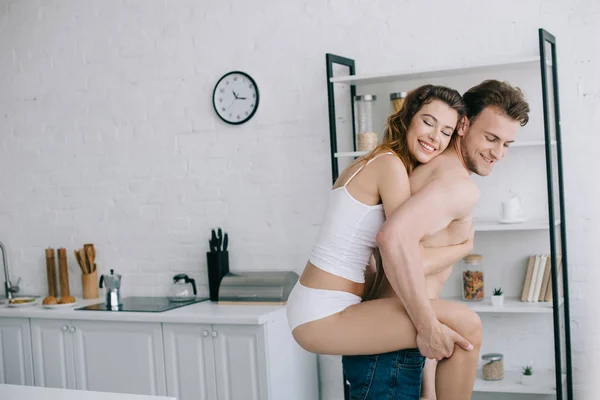 Bonito namorado piggybacking seu sorrindo e atraente namorada no apartamento — Fotografia de Stock