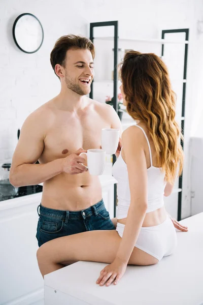 Girlfriend and handsome boyfriend smiling and holding cups with tea in apartment — Stock Photo