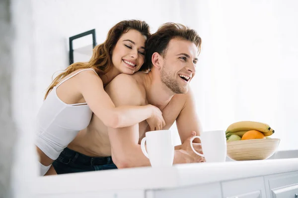 Attraente fidanzata e bello fidanzato sorridente e abbracciare in appartamento — Foto stock