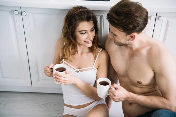 High angle view of attractive girlfriend and handsome boyfriend smiling and holding cups in apartment — Stock Photo