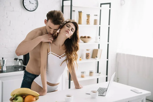 Atractiva novia con los ojos cerrados y novio guapo abrazándose en el apartamento - foto de stock