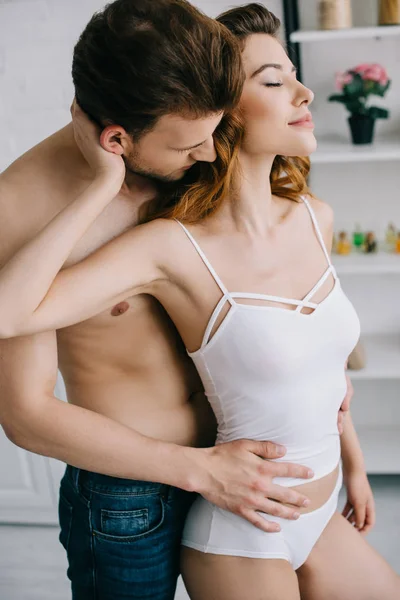 Bello fidanzato abbracciare attraente fidanzata con gli occhi chiusi in appartamento — Foto stock