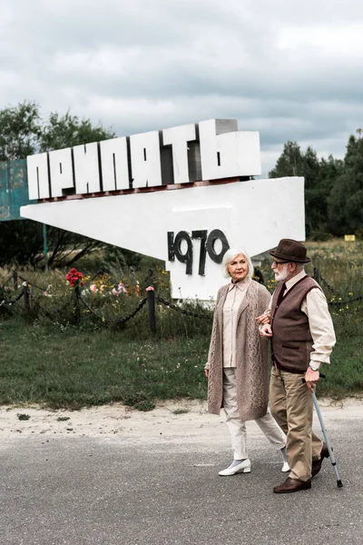 PRIPYAT, UCRAINA - 15 AGOSTO 2019: marito e moglie in pensione che camminano vicino al monumento con lettere di pripiato — Foto stock