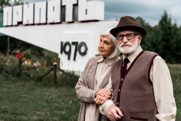 PRIPYAT, UKRAINE - AUGUST 15, 2019: retired husband and wife standing near monument with pripyat letters — Stock Photo