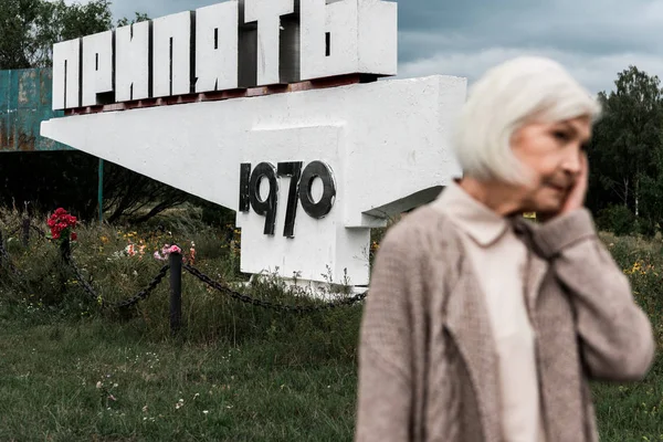 PRIPYAT, UCRAINA - 15 AGOSTO 2019: donna in pensione in piedi vicino al monumento con lettere di pripiato — Foto stock