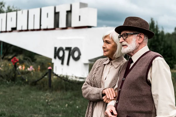 Pripjat, ukraine - 15. August 2019: Rentnerehepaar steht neben Denkmal mit Pripjat-Buchstaben — Stockfoto